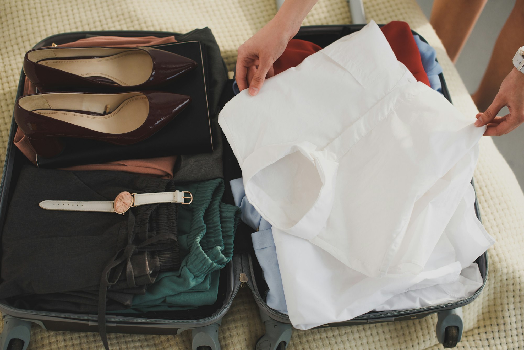 cropped view of businesswoman packing clothes in suitcase for business trip
